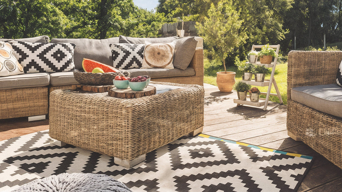 Stylish outdoor wicker sofa and coffee table set on a wooden deck with a geometric rug, showcasing 3 perfect pieces of outdoor furniture for any home.