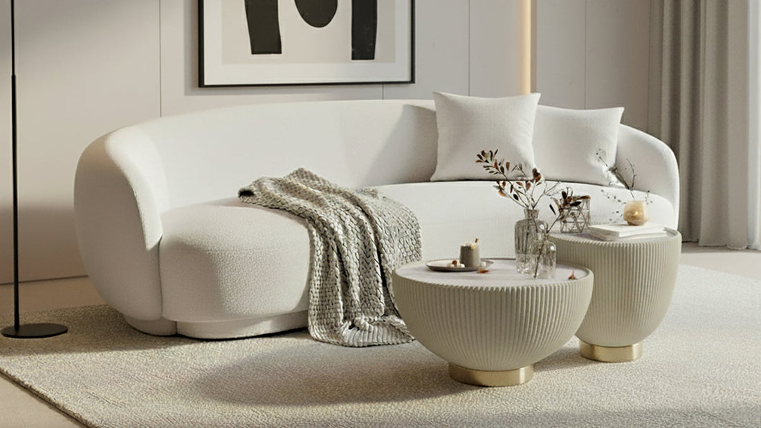 Janelle 213cm Curved Bouclé 3.5-Seater Sofa in Cream White, featuring plush throw pillows, a beige knitted blanket, and a solid wood frame, set in a minimalist living area.