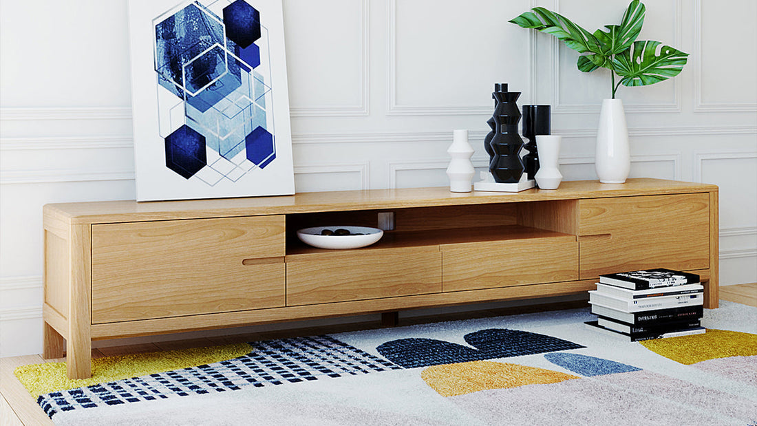 Long oak media cabinet featuring open shelving and drawers, decorated with a potted palm leaf against a classic white panelled wall background.