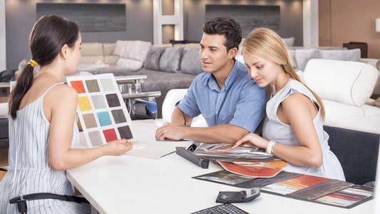A couple reviewing fabric and color swatches with a salesperson in a furniture showroom, illustrating the new guide to furniture trends this year.