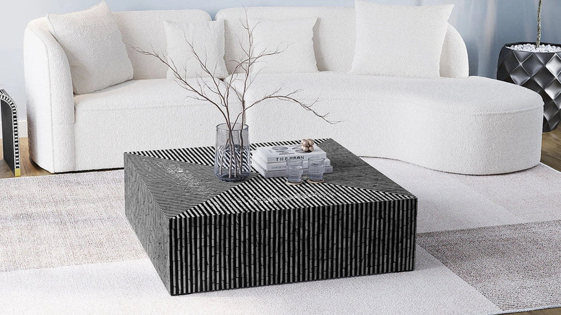 A square black and white striped coffee table with a vase and books, placed in front of a curved white boucle sofa on a neutral rug.