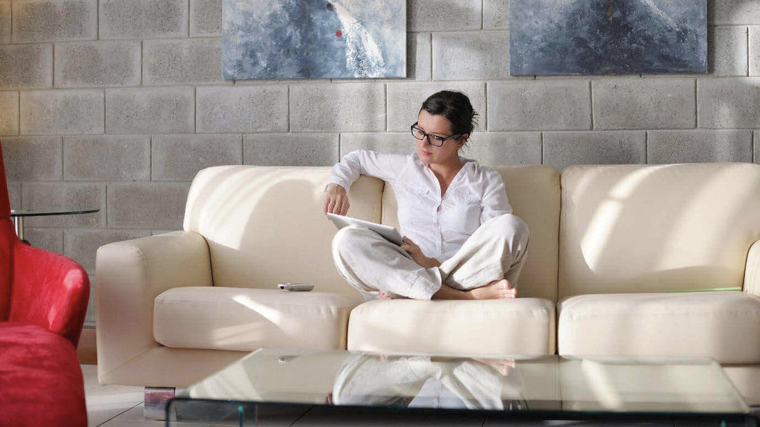 Woman sitting comfortably on a cream-colored sofa and using a tablet to research how to choose the right sofa for her home.