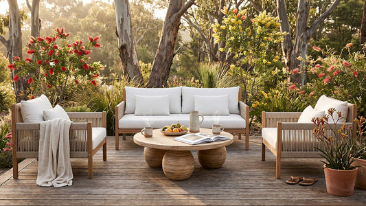Sun-drenched Australian backyard — a beautifully styled outdoor lounge setting with plump, clean cushions in warm sand and white tones, surrounded by greenery and timber decking