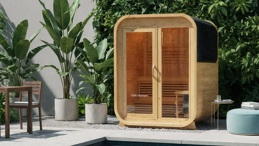 Waru 3 Person Traditional Finnish Outdoor Sauna in Natural, featuring a pod-shaped wooden design with a glass front, visible interior bench seating, and situated on a gravel patio beside a plunge pool.