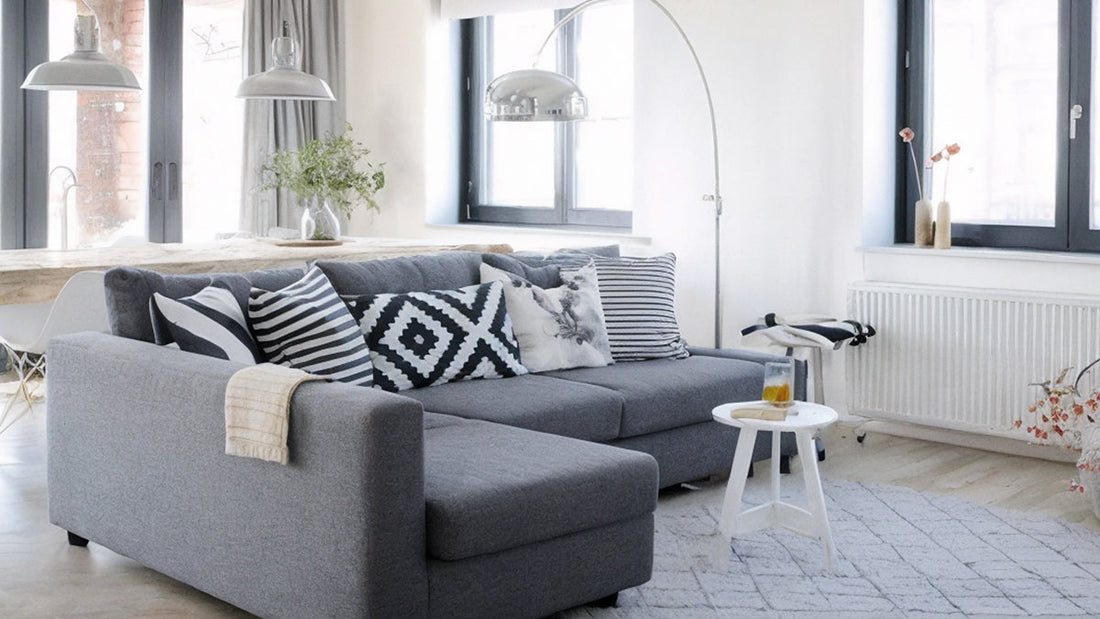 Modern gray sectional sofa bed with throw pillows in a bright, minimalist living room, highlighting a must-have piece for maximizing space and guest comfort.