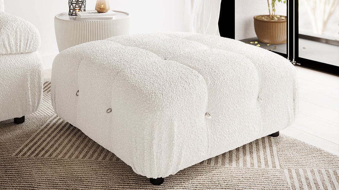 Keila Modular Tufted Boucle Ottoman in Cream White, featuring tufted channels and metal ring accents, placed on a neutral rug in a minimalist living room with a ribbed side table and sheer curtains.
