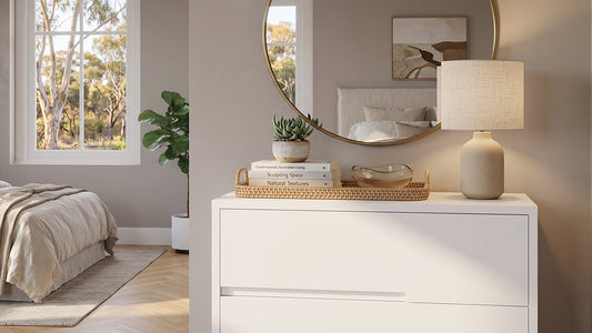 White chest of drawers with round mirror and table lamp in bright bedroom