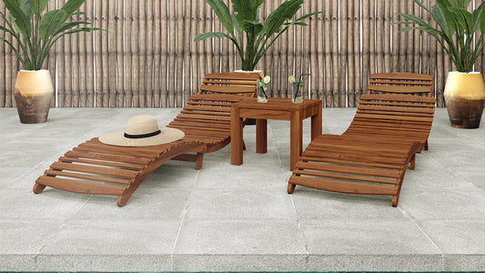 Wave Hardwood Acacia Outdoor Sun Loungers Set of 2 in Natural, featuring curved designs on a tiled deck with a side table, iced drinks, a straw hat, and tropical plants in the backdrop.