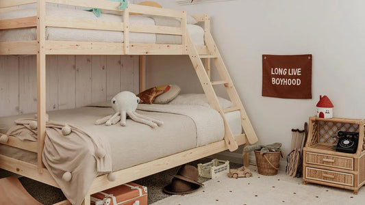 Scandinavian-style children's room featuring a light wood bunk bed with neutral bedding, a knitted octopus toy, under-bed storage, a woven cabinet, and a Long Live Boyhood wall hanging.