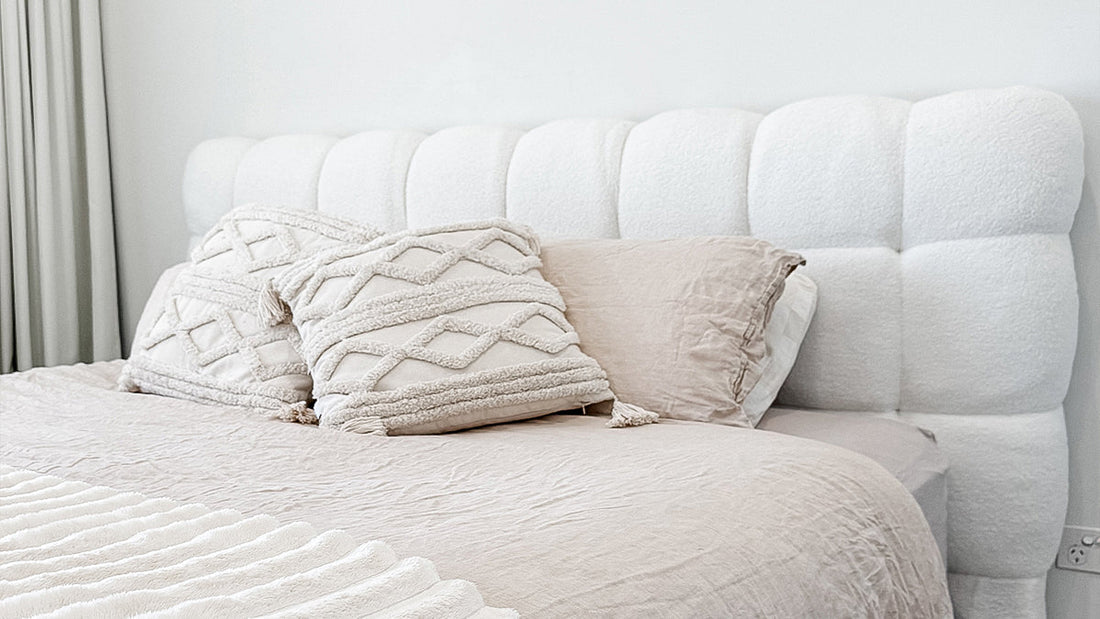 Nikias Super King Boucle Fabric Bed Frame in Cream White features a grid-tufted headboard, neutral-toned bedding, textured pillows, and a ribbed throw, creating a luxurious, monochromatic bedroom scene.