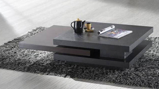 Modern dark gray geometric coffee table on a shag rug with a black teapot and magazine, reflecting contemporary personality in furniture.