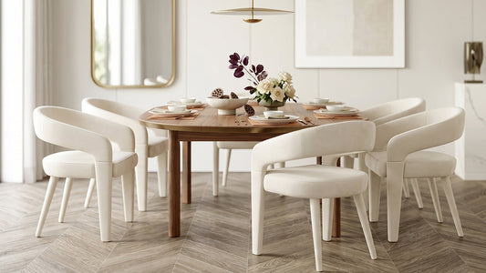 A modern dining set comprising a circular wooden table paired with four off-white upholstered dining chairs featuring curved backrests and continuous arm supports, arranged on a herringbone-patterned floor in a bright, minimalist dining room.