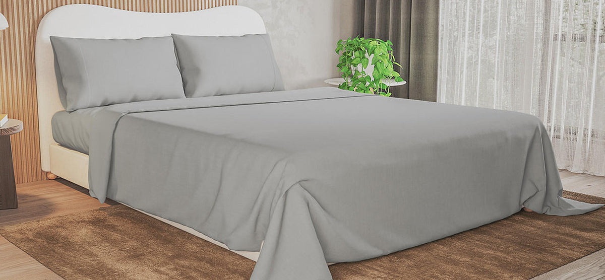 A neatly made bed with light gray sheets and pillows, white curved headboard, wood-slat accent wall, brown rug, and a nightstand with a green plant.