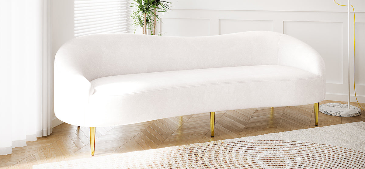 Bright living space with a curved white sofa on herringbone floor, accented by a textured rug, tall plant, and arcing gold floor lamp with a marble base.