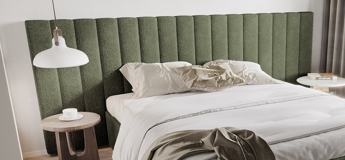 Modern bedroom with an olive-green upholstered headboard, white bedding, neutral-beige pillows, a wooden side table with a cup, and another with books, softly lit from the right.