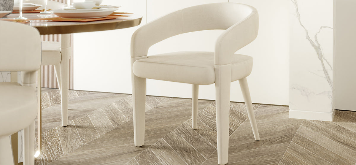 A modern dining-room corner featuring a cream-colored upholstered chair with a curved back, next to a round table set with white dinnerware on russet placemats.
