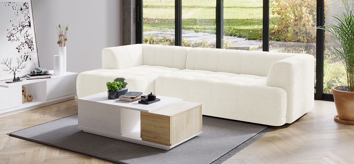 Contemporary living room with off-white sectional sofa, two-tone coffee table, gray rug, black-framed windows, and minimalist decor. Features potted plants and light herringbone wood floor. Scandinavian style.