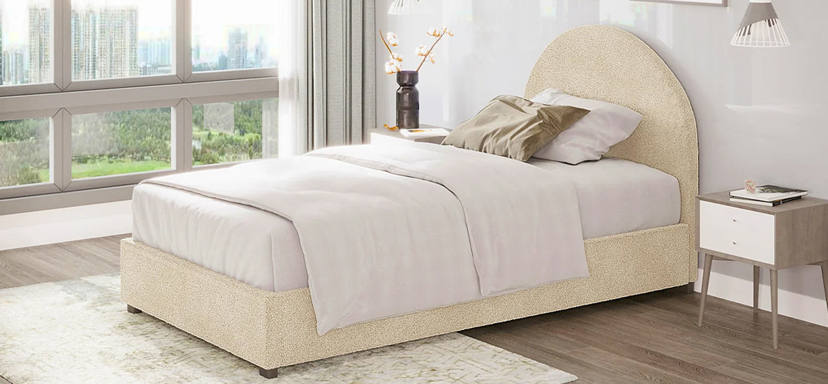 Minimalist bedroom with a low-profile upholstered bed, arched headboard, white and cream bedding, wooden nightstand, pendant lights, and window view of greenery and skyline.