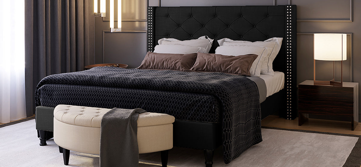 Modern bedroom showcasing a large bed with a quilted dark headboard, layered white and taupe-brown bedding, a wooden nightstand with a lamp, and floor-to-ceiling curtains.