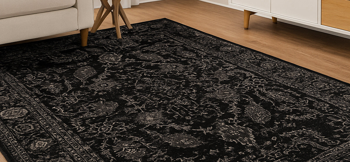 Dark patterned area rug with light decorative motifs on wood floor, framed by sofa legs, a wooden side table, and a white and wood console.