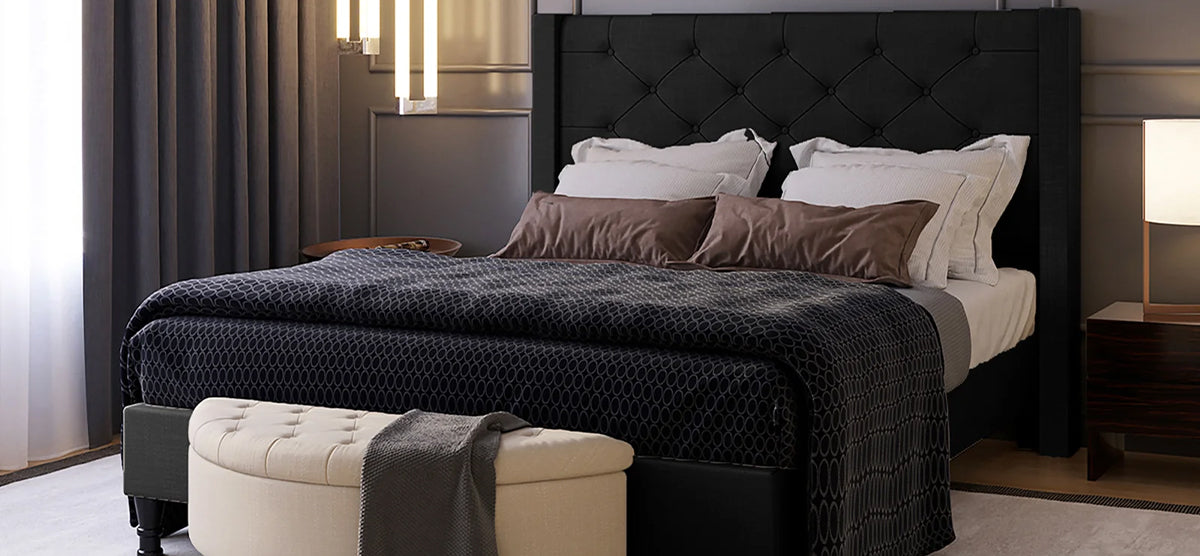 Modern bedroom with a dark-upholstered, tufted-headboard bed, white sheets, brown pillows, patterned duvet, light bench with throw, wooden nightstand, table lamp, and pendant lights.