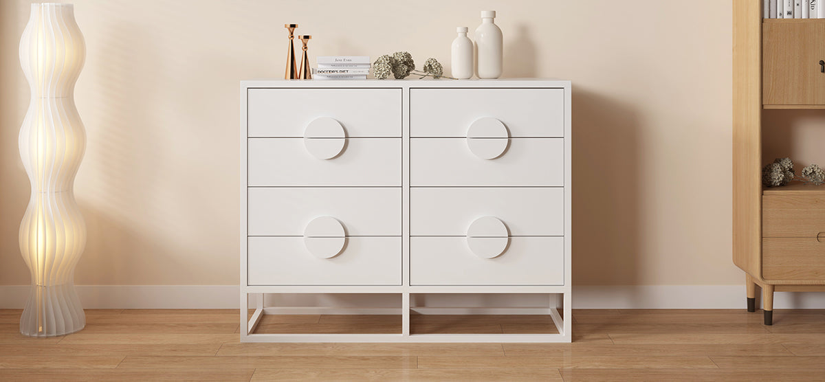Minimalist interior with a white double-dresser featuring oversized pulls, topped with books, metallic candleholders, dried hydrangea, and ceramic vases; adjacent to a glowing undulating floor lamp.