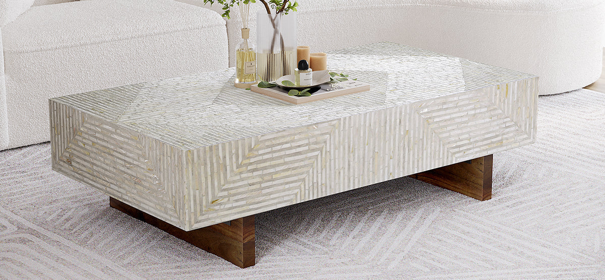 Rectangular coffee table with mother-of-pearl inlay top, wooden legs, featuring a tray with decorative items and a ribbed glass vase, in a modern living room setting.