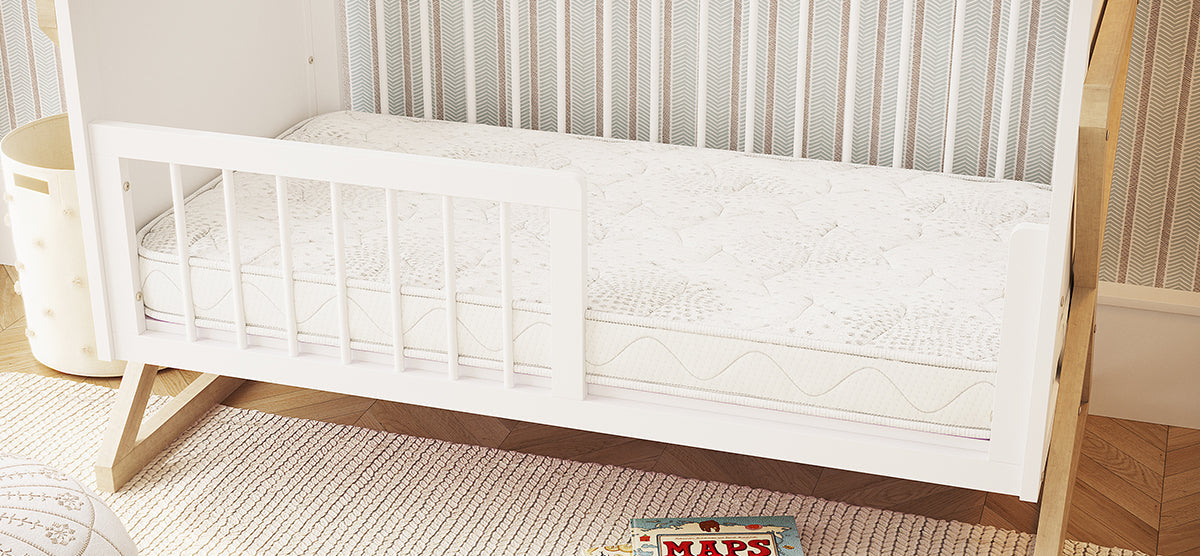 A softly lit children's room corner with a white toddler bed, natural-wood support, off-white rug, tufted storage bin, floor pouf, and an open MAPS book.