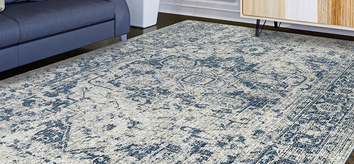 Vintage-style ivory and muted blue area rug on dark wood floor, partially under a dark blue sofa and adjacent to a light wood sideboard.