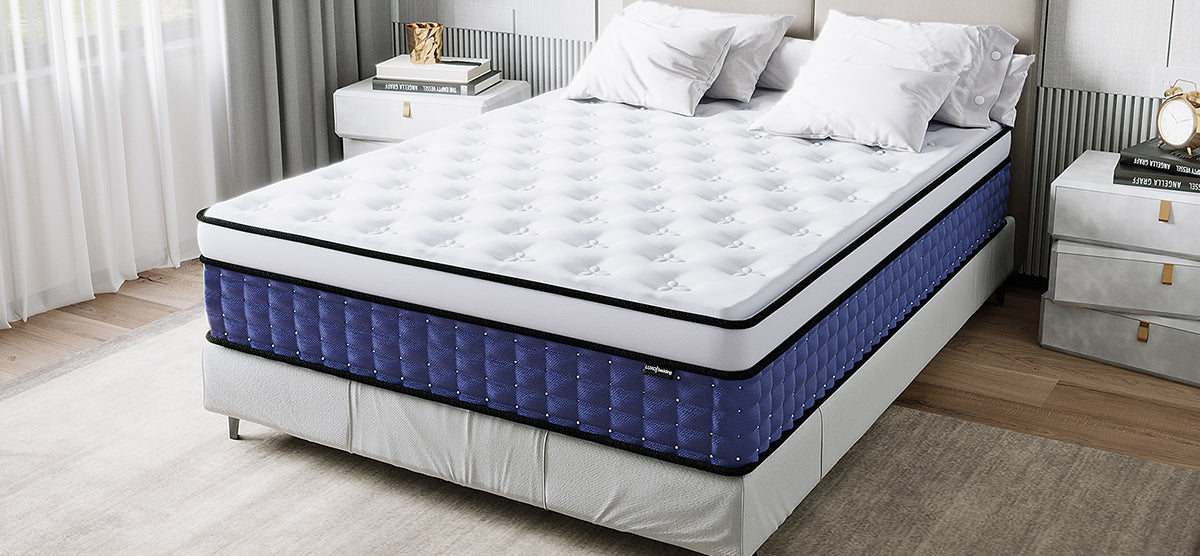 Neatly made bed featuring a two-tone mattress with a white top and deep blue sides, flanked by bedside cabinets with books, in a softly lit bedroom with sheer curtains.