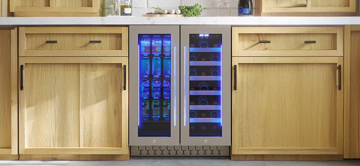 Under-counter dual-zone beverage cooler with stainless steel-framed glass doors, left side with canned drinks, right side with wine bottles, under a white countertop with kitchen items.