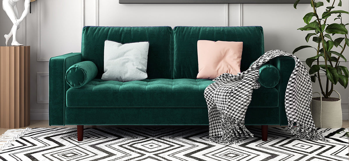 Emerald-green sofa with matching bolster pillows, minty blue and blush pink throw pillows, houndstooth throw, geometric rug, potted plant, and classical sculpture on a pedestal.