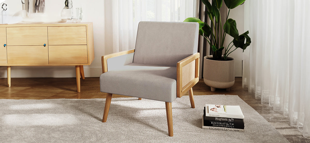 A minimalist living-room corner with a mid-century armchair, light-wood sideboard, neutral rug, stack of books, tall potted plant, and sheer curtains filtering daylight.