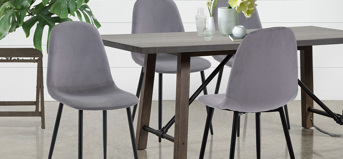 Minimalist dining area featuring a dark-wood table with black metal legs, four gray upholstered chairs, decorative items, and a Monstera plant against a white paneled wall.