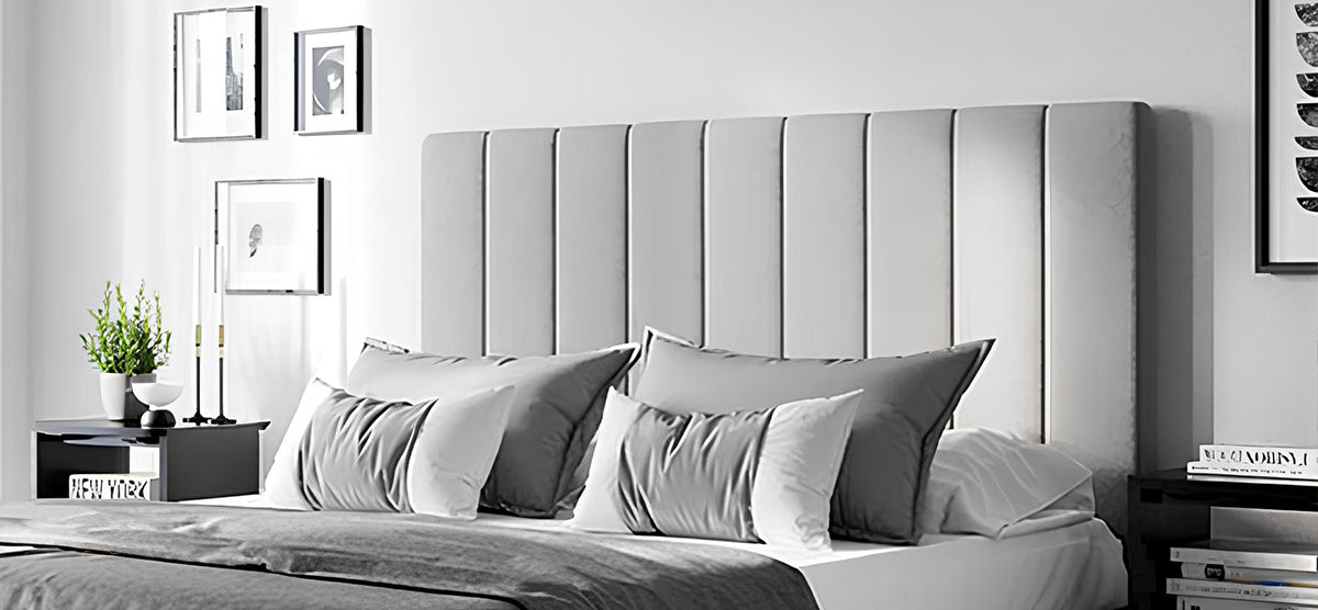 Modern bedroom with a large upholstered bed featuring a channeled headboard, layered gray and white bedding, flanked by nightstands with decor, and framed art on the wall.