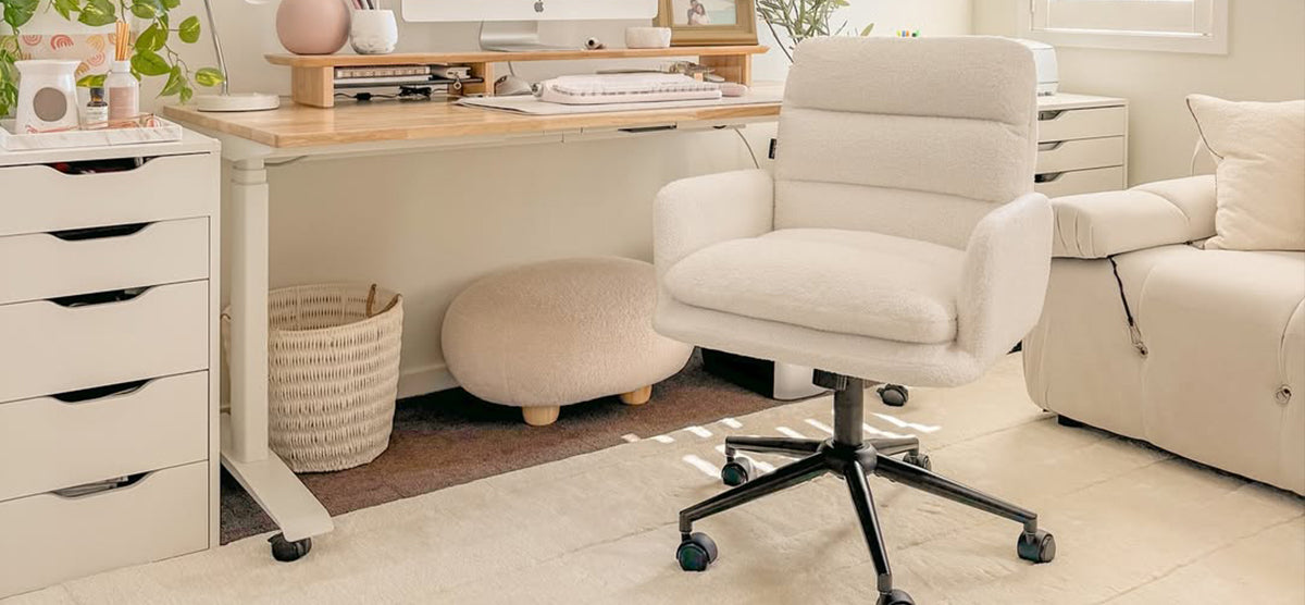 A cozy, neutral-toned home office with a height-adjustable wooden desk, iMac, plush swivel chair, white storage unit, seagrass basket, and decorative plants.