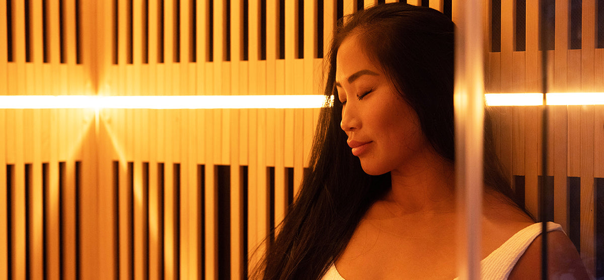 A serene young woman wearing a light towel relaxes in a warm, wood-paneled sauna with soft, amber lighting, creating a tranquil spa-like atmosphere.