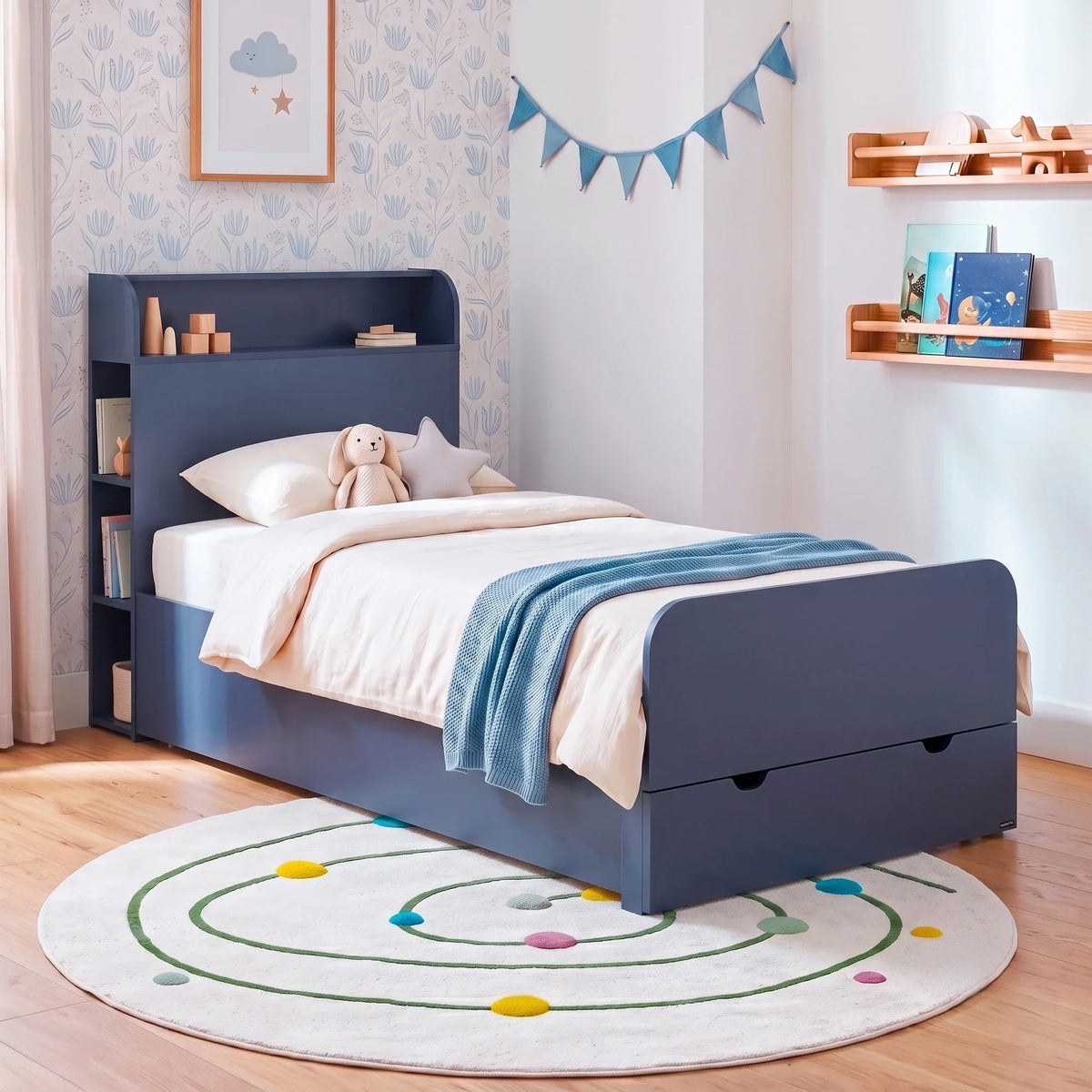 Children’s bedroom corner with a natural‐pine twin-over-full bunk bed, featuring a slanted ladder, safety rails, built-in drawers, blueish bedding, stuffed animals, and a pennant banner.
