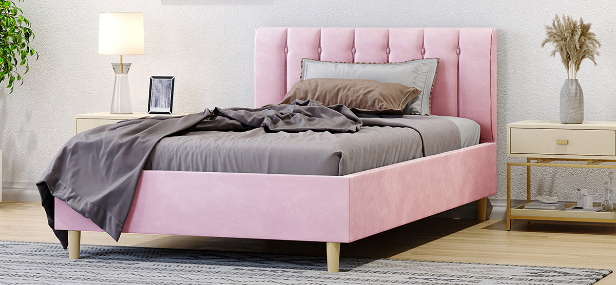 Modern bedroom with a plush pink-upholstered platform bed featuring a vertically tufted headboard, grey bedding, and light-wood nightstands with decor, set on a light wood floor.