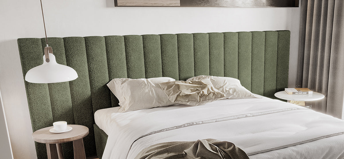 Modern minimalist bedroom with an olive-green upholstered headboard, white linens, and neutral pillows. Features side tables with a coffee cup, books, and abstract wall art above.