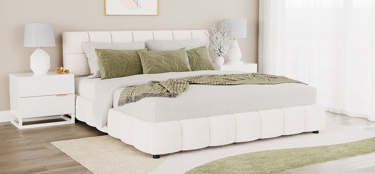 A contemporary bedroom featuring an upholstered platform bed in off-white boucle with a tufted headboard, gray bedding, olive-green pillows, and nightstands with white lamps and decorative accents.
