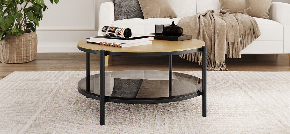 Cozy living-room setup featuring a round, two-tier coffee table with a light wood top, black metal legs, and a tinted glass shelf, surrounded by a sofa, throw blanket, and houseplant.