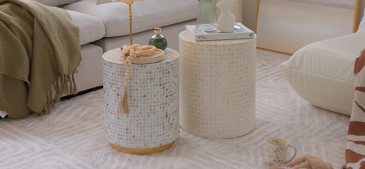 Neutral-toned living area with mosaic-tiled side tables; one with wooden beads and glass vase, the other with books and ceramic vase. Sofa and chair with throws and cushions.