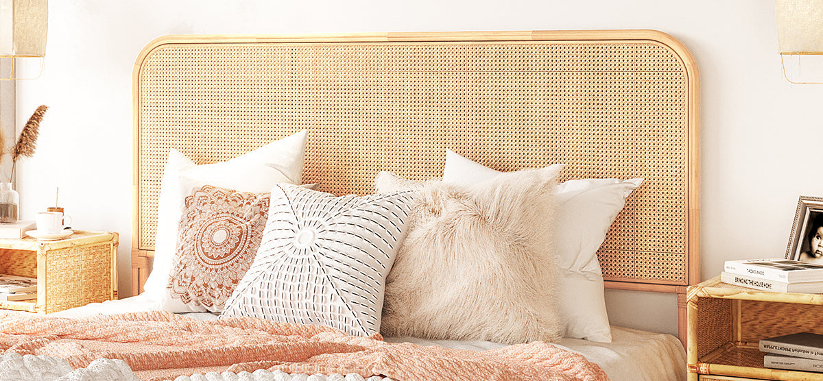 Cozy boho bedroom with rattan headboard, decorative pillows, peachy-pink throw blanket; matching nightstands hold a coffee cup, vase with dried grasses, books, and a framed photo.