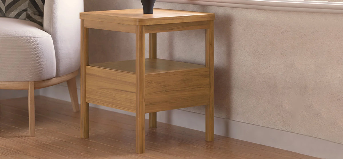 Wooden side table with square legs beside a light sofa, featuring a lower drawer, open shelf, and topped with a simple black vase.