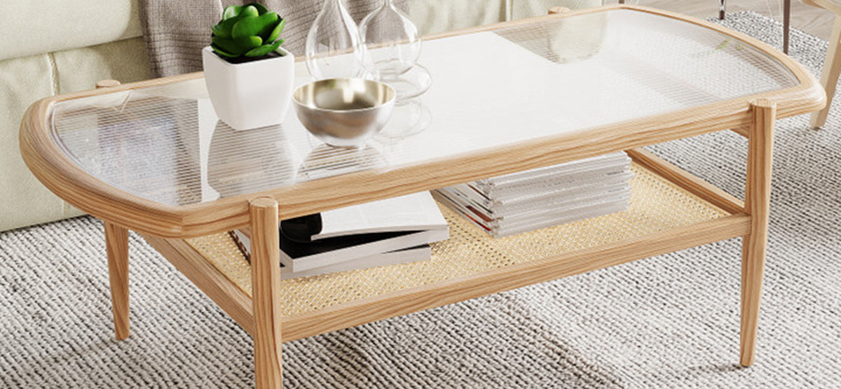 Mid-century-style coffee table with light wood frame and glass top, featuring a succulent in a planter, metallic bowl, glass vases, and magazines on a rattan shelf.