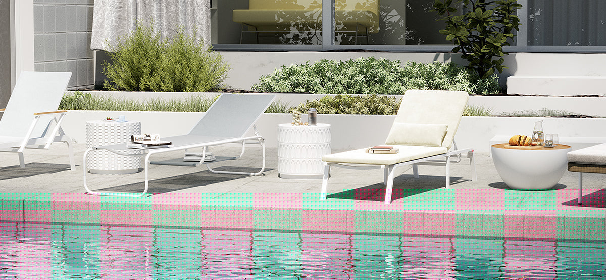 Modern pool-side terrace with three white lounge chairs, side tables holding decor, drinks, and a loaf of bread, near a clear blue swimming pool.