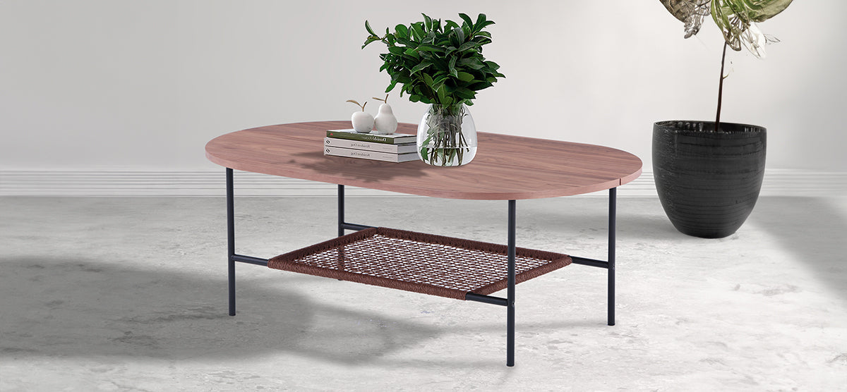 Minimalist modern coffee table with an oval wooden top, thin black metal legs, and a woven shelf, decorated with books, pear sculptures, and a glass vase with greenery.