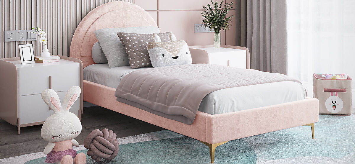 Pastel-themed children's bedroom corner featuring a blush-pink upholstered bed, star and animal pillows, white nightstands, light-blue rug, plush bunny toy, and a cartoon bunny toy bin.