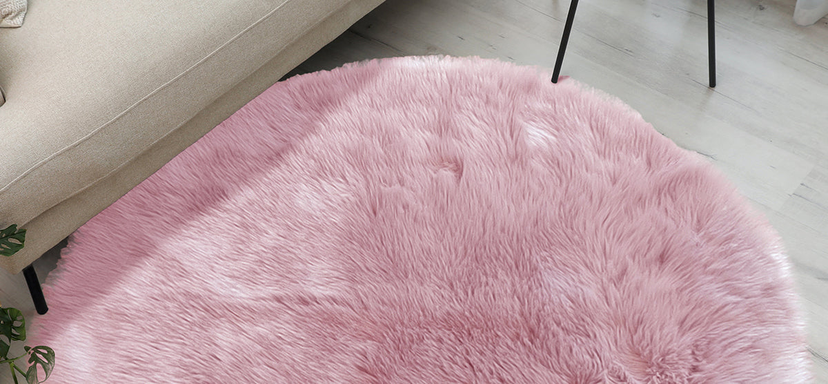 Pale pink shag rug on light wood floor, partially under a beige sofa and black chair leg, with a small houseplant in the corner.